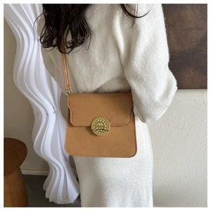 Detail view of a camel leather crossbody bag with a large embossed vintage gold buckle