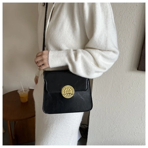 Close-up of vintage black leather crossbody bag with textured gold round buckle detail