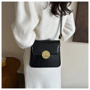 Detailed back view of a minimalist black leather crossbody bag with a golden round buckle