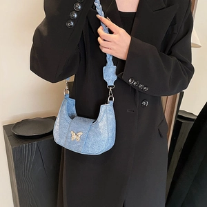 Detailed view of light blue denim saddle bag featuring a gold butterfly buckle and braided strap