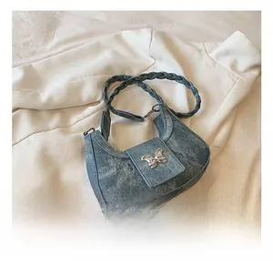 Detail of blue denim crescent bag featuring silver butterfly buckle and woven strap