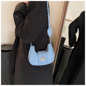 Detail of light blue denim crescent bag with gold butterfly clasp and woven shoulder strap