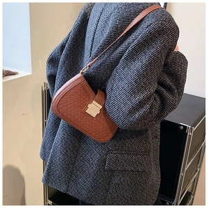 Detail of a brown woven shoulder bag with golden metallic clasp on an oversized blazer
