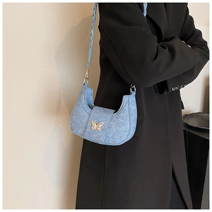 Close-up of denim crescent shoulder bag featuring a gold butterfly buckle and woven strap