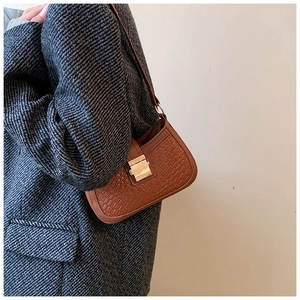Close-up of brown woven shoulder bag with gold buckle on model in grey winter coat