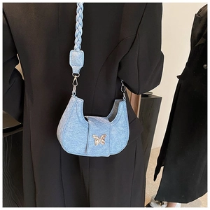 Detail of light blue denim underarm bag with golden butterfly buckle and braided strap