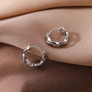 Double-layered Mobius silver hoop earrings with a polished wavy twist on brown fabric