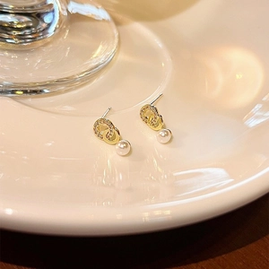 Close-up of golden bow-knot pearl earrings with zircon inlay on a cream ceramic plate