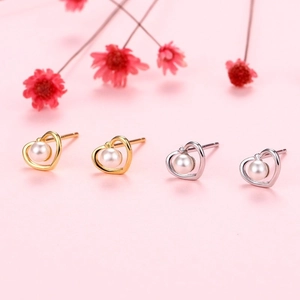Detailed close-up of hollow heart-shaped earrings with central pearl on pink background
