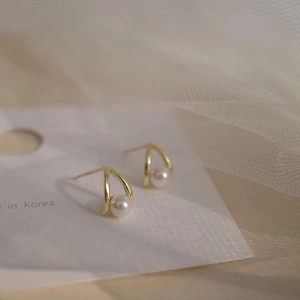 Detail of elegant gold bow earrings with white pearls on a soft white tulle background