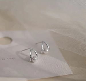 Detail of silver bow pearl earrings featuring polished metal curves and lustrous white pearls