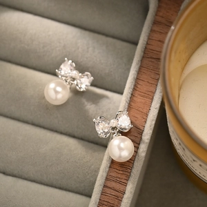 Elegant silver bow pearl earrings with cubic zirconia shown on a velvet jewelry tray