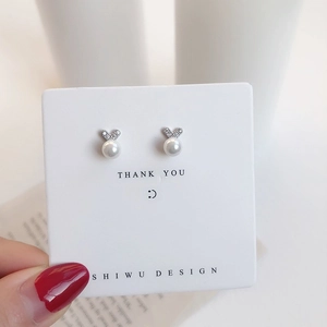 Detail of bow-shaped pearl stud earrings with sparkling zircons on a white display card