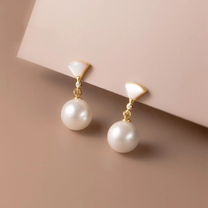 Elegant gold bow earrings with white shell fans and lustrous pearls on a pink stand