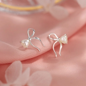 Macro shot of silver bow stud earrings with heart-shaped pearl on pink silk background