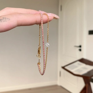 Detail of double-layer gold bracelet featuring pink zircon stones and a four-leaf clover charm