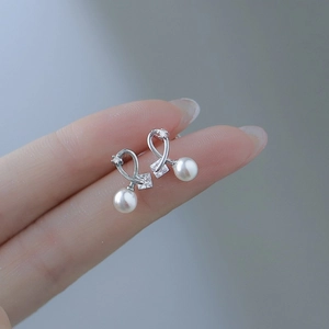 Detail of silver bow earrings with square zircon and hanging white pearl on fingertips