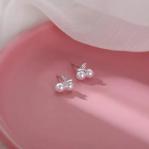 Macro detail of silver cherry earrings with white pearls on a pink ceramic dish