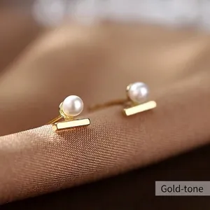 Detailed close-up of a gold pearl stud earring on a soft silk fabric background