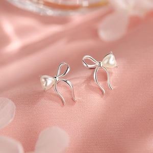 Macro shot of silver bow earring with heart pearl inlay on pink silk fabric background