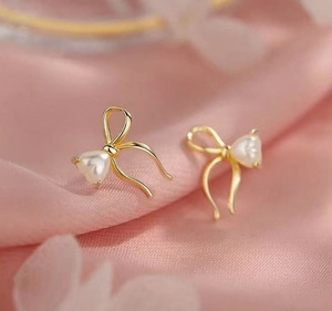 Detail of elegant gold bow earrings with heart-shaped pearls on soft pink silk fabric