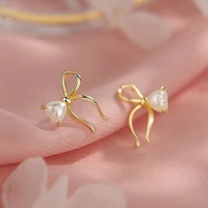 Elegant gold bow earrings with heart pearl center on pink satin background