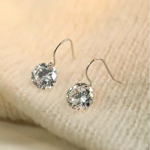Vue macro détaillée de boucles d'oreilles en argent et zircon sur maille beige