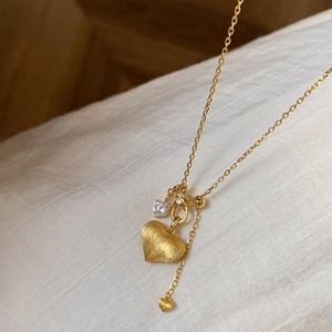 Macro detail of gold brushed heart pendant with sparkling diamond accent and chain