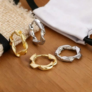 Close-up of twisted spiral hoop earrings in gold and silver finish on a wooden surface