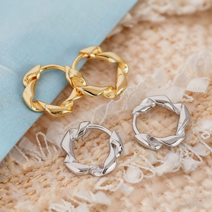 Macro detail of twisted geometric hoop earrings in polished gold and silver finishes