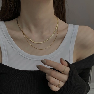 Detail of layered gold snake chain and thin necklace worn by a model for a chic look
