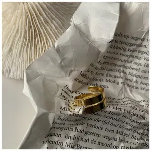 Dettaglio dell'anello dorato a doppia spirale su carta materica con ombre artistiche