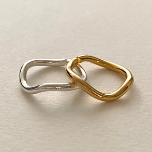 Minimalist irregular wavy rings in gold and silver set on a light grey texture background