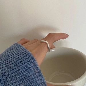 Minimalist silver wavy curve ring on a model holding a cup for a stylish lifestyle look