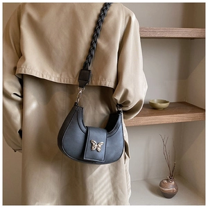 Detail of black crescent shoulder bag with butterfly metal clasp and woven strap on model