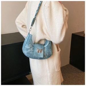 Detail of light blue denim crescent bag featuring a metallic butterfly clasp and woven strap