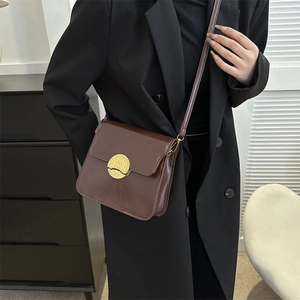 Minimalist dark brown leather crossbody bag with round gold buckle on a black blazer
