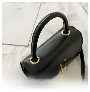 Detail of a black matte cylinder bag with gold hardware and top handle on white fabric