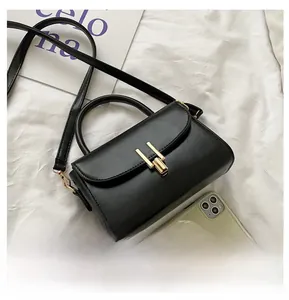 Detail view of small black crossbody bag with gold buckle next to a smartphone for size
