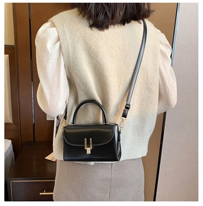 Detail of a black glossy leather crossbody bag with a gold buckle and round handle