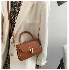 Detail of a brown leather crossbody bag with a gold H-clasp on a white suit model