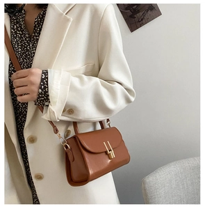 Detail of caramel brown leather mini square bag with golden metallic clasp and top handle