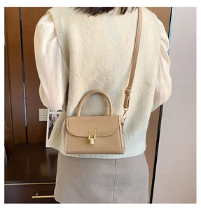 Rear view of a model wearing a beige crossbody bag with a gold metal lock and handle