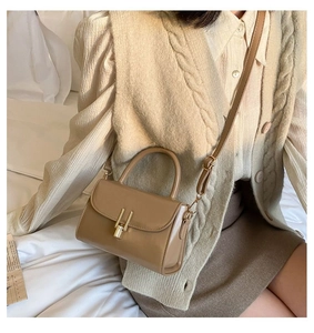 Detail of khaki square bag with golden lock and adjustable strap on a neutral setting