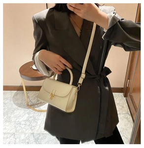 Detail of cream rectangular bag with golden metal buckle and leather handle texture