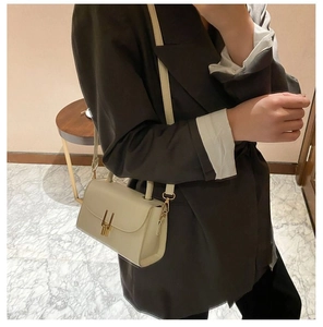 Detail view of cream leather shoulder bag featuring a minimalist gold U-shaped magnetic clasp