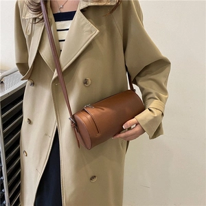 Detail of a vintage dark brown cylindrical crossbody bag on a model in a trench coat
