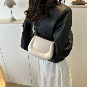 Close-up of a cream leather saddle bag styled with a black leather jacket and white skirt