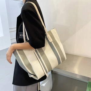 Dettaglio della borsa tote in tela a righe con manici in pelle portata a spalla