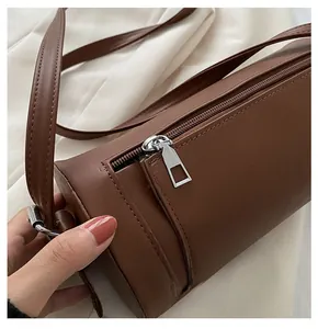 Detailed close-up of smooth silver zipper and fine stitching on a brown cylinder bag